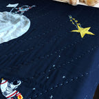 Navy blue quilted pillow featuring stitched appliqué of yellow stars and a rocket; ideal for space-themed kids' bedding, toddler galaxy room decor, or astronaut nursery accents.



