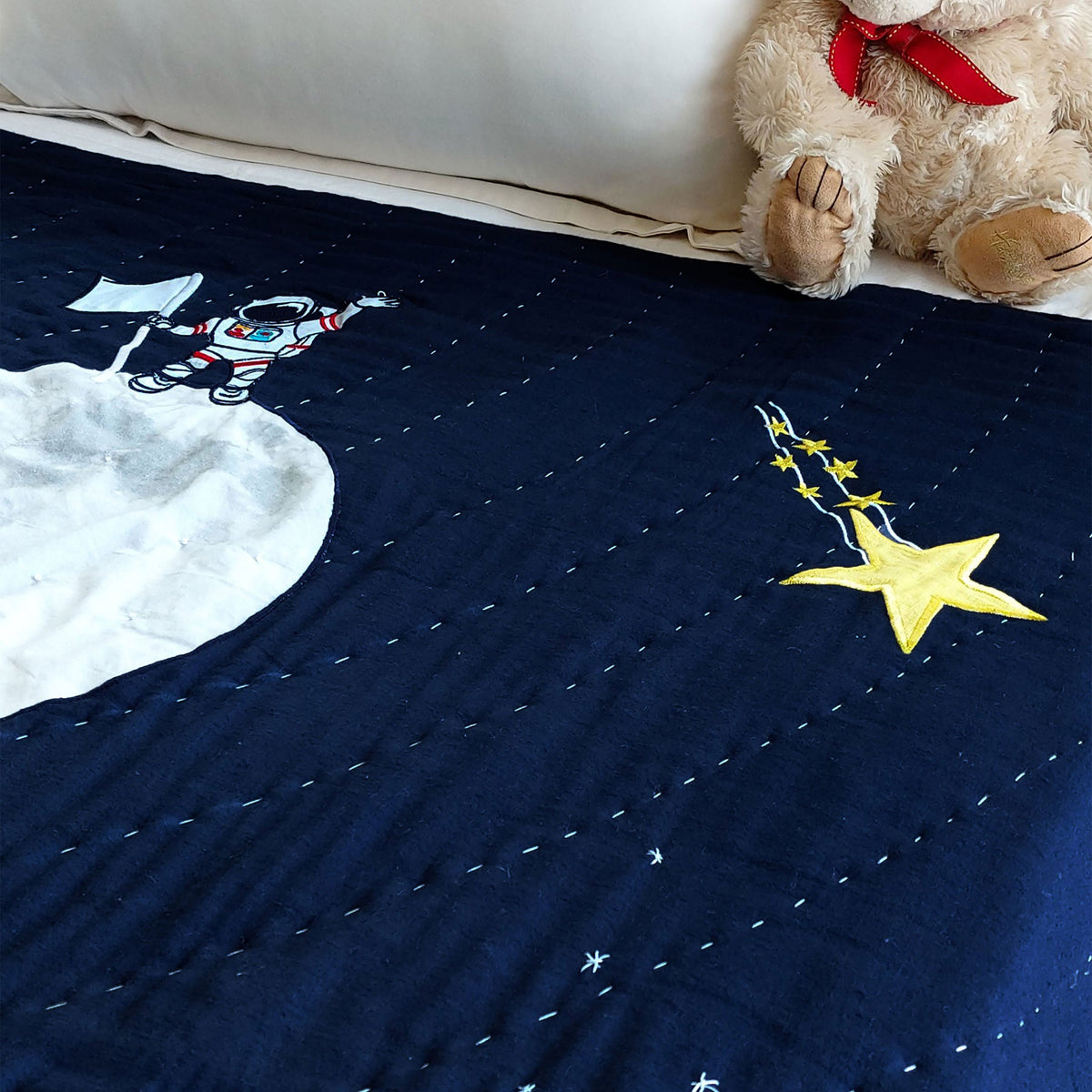 Close-up of navy space-themed quilt showing stitched appliqué astronaut on soft cotton fabric; perfect for toddler bedding, space-themed nursery, or kids’ room with galaxy decor.




